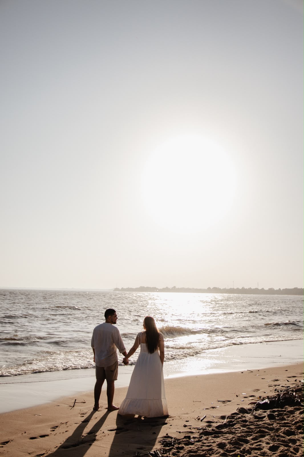 Aline e Artur de mãos dadas olhando o pôr do sol